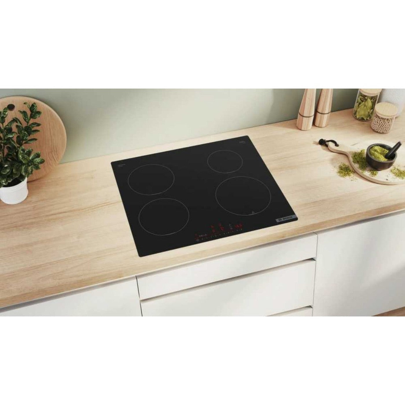 Une plaque vitrocéramique noire à quatre zones de cuisson sur un plan de travail en bois.