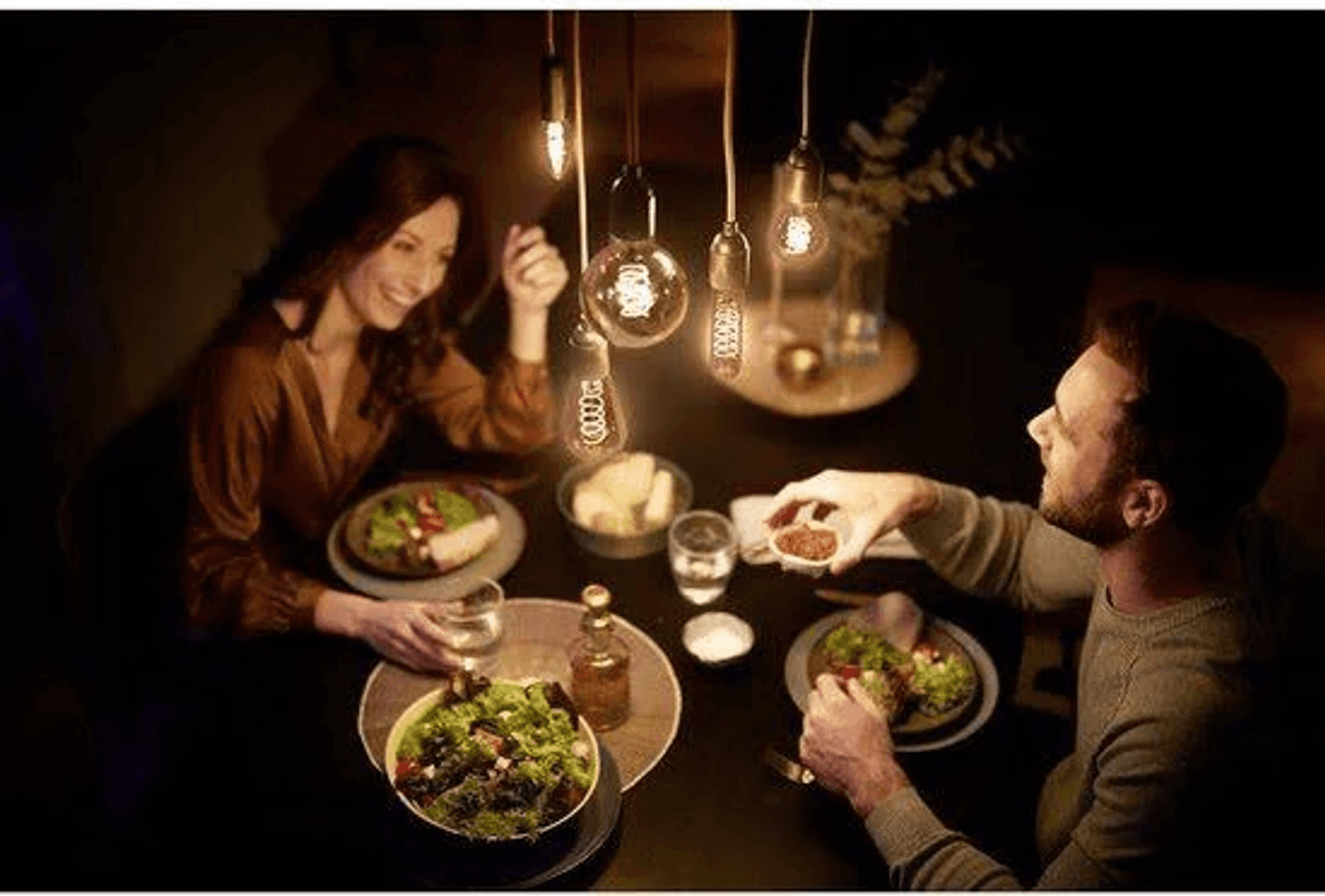 A couple eats dinner by candlelight, with food on the table.