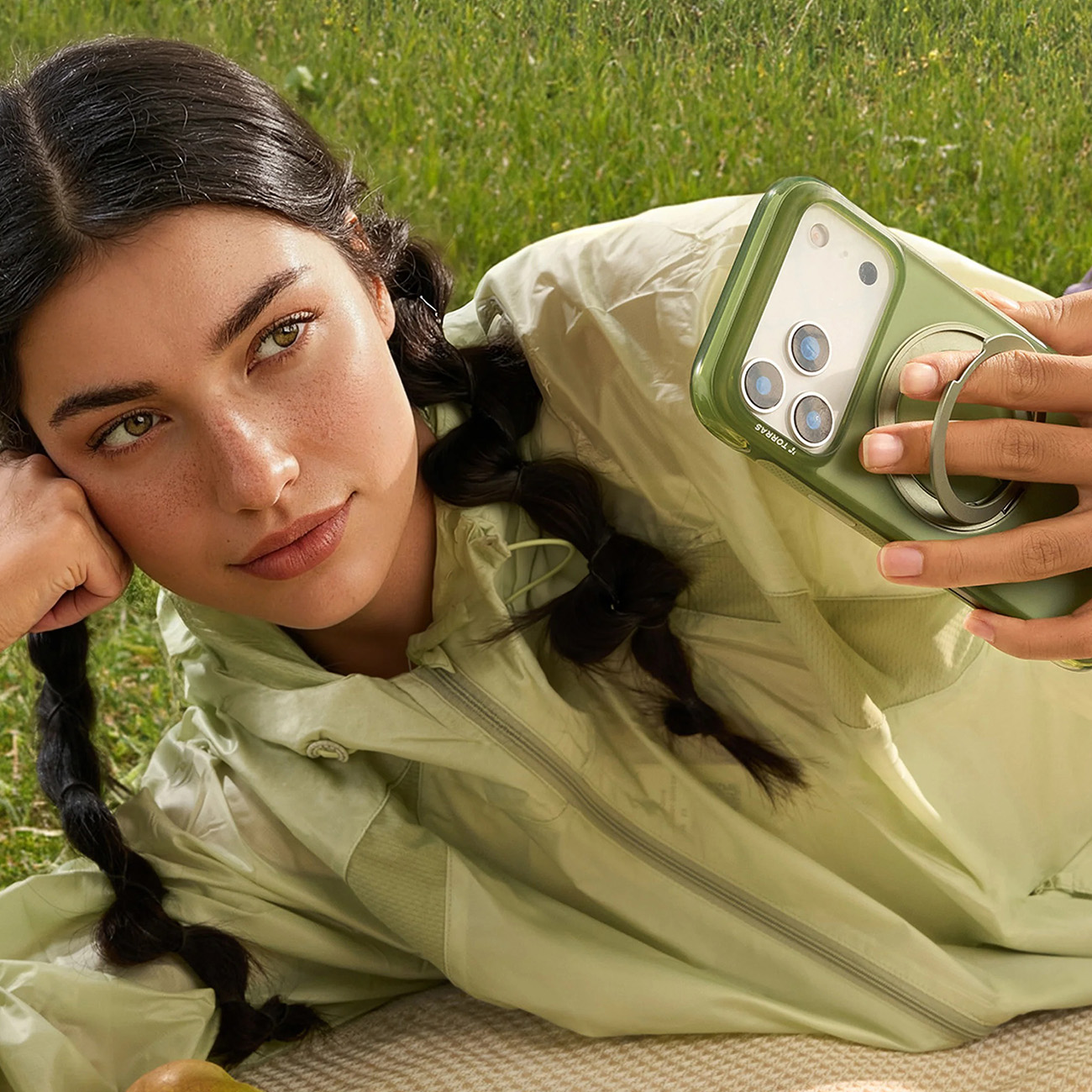 Mujer tumbada en la hierba sujetando un teléfono verde con soporte de anillo.