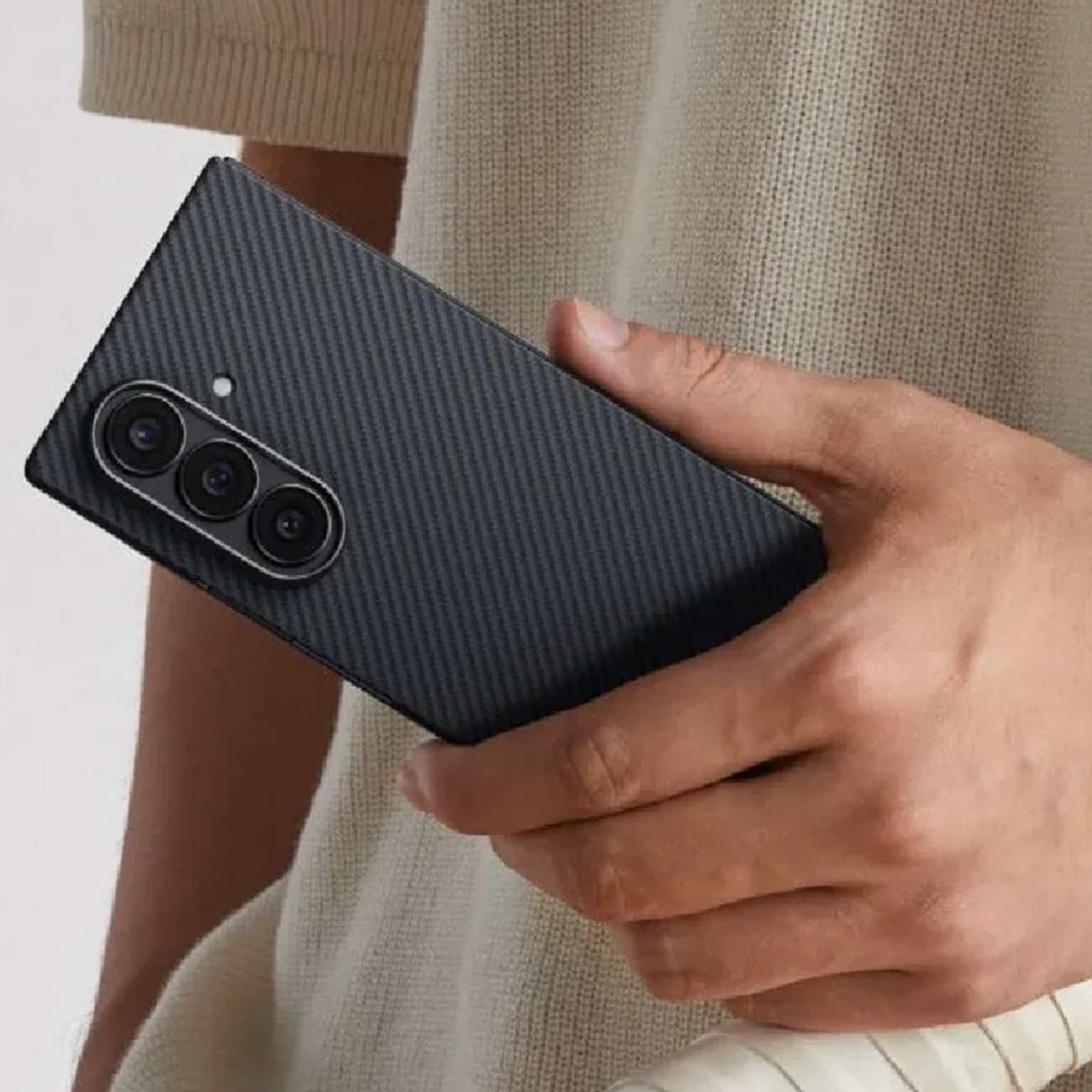 Mano sosteniendo un smartphone negro con tres cámaras y textura de carbono.