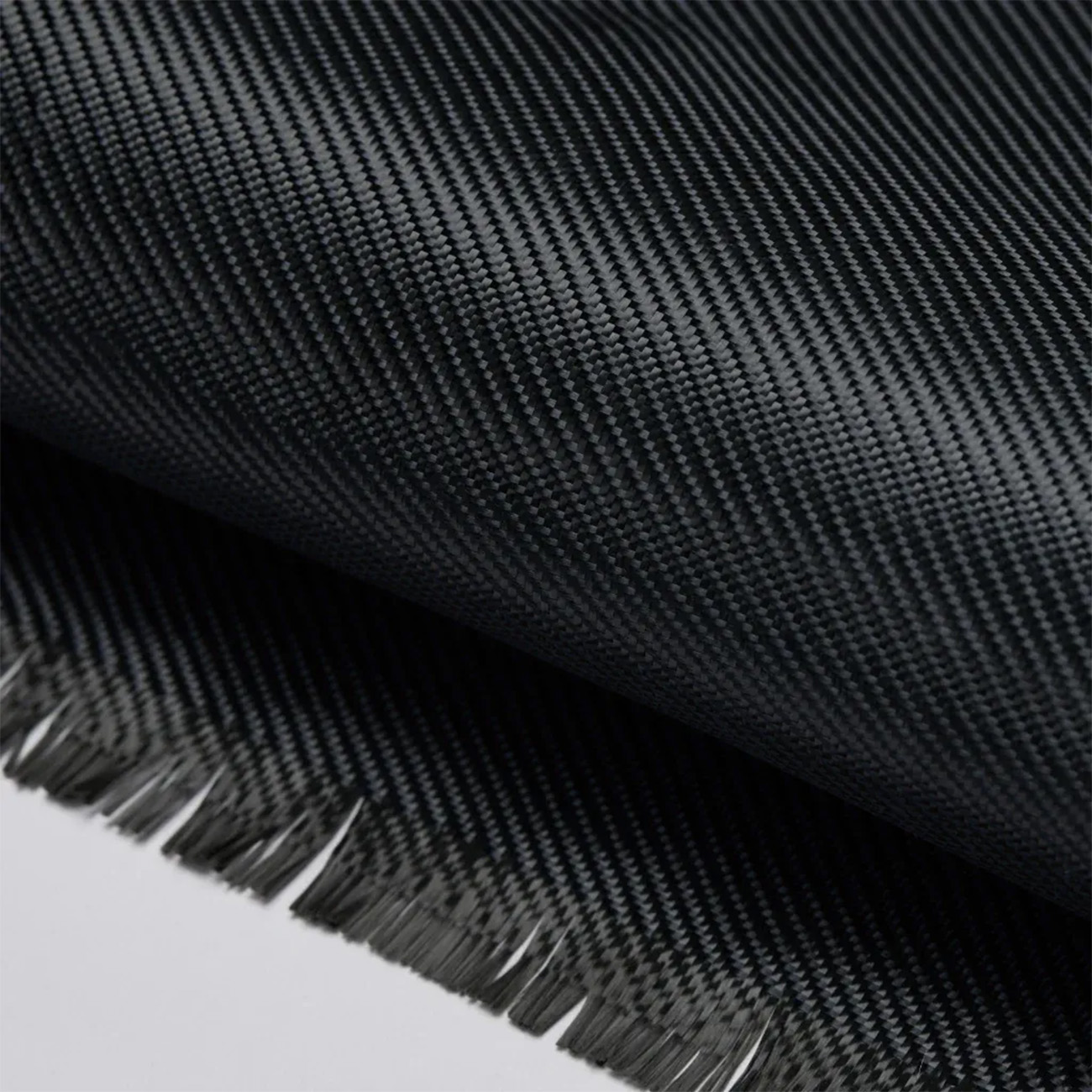 Tejido de fibra de carbono negro con patrón de tejido visible y bordes deshilachados.