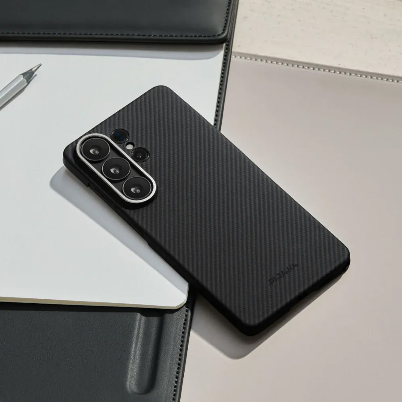Un teléfono negro con patrón de carbono sobre cuadernos, con un bolígrafo al lado.