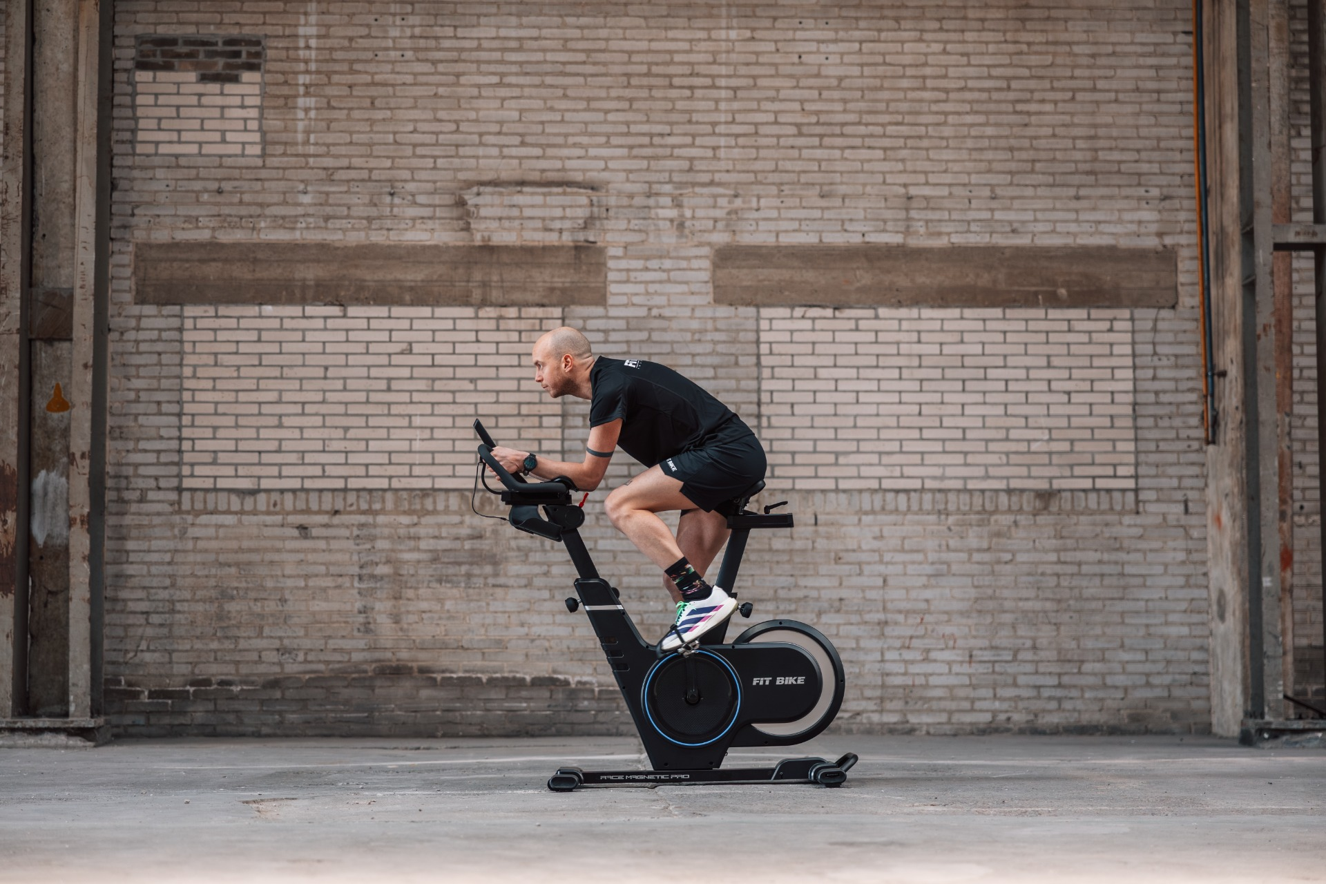 Un homme fait du vélo d'appartement devant un mur de briques.