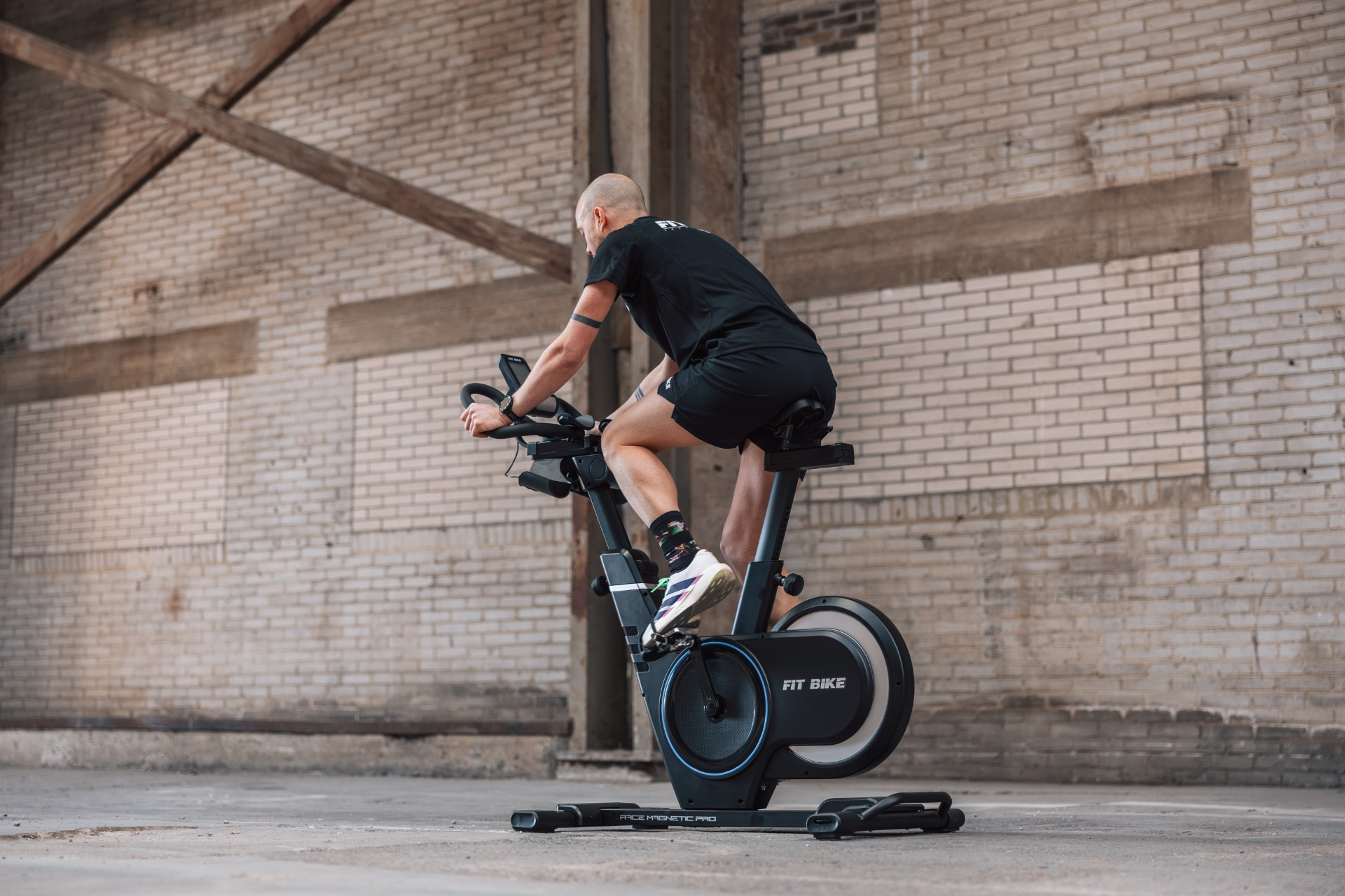 Un homme sur un vélo d'appartement noir dans un hall en briques.
