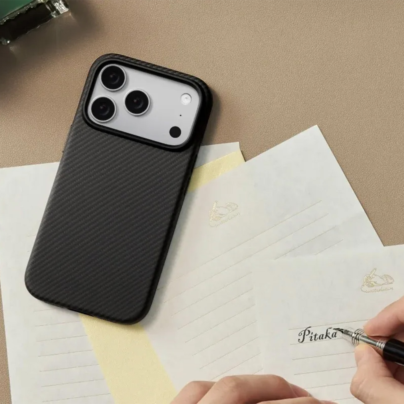 Schwarzes Handy mit Carbon-Hülle auf Notizblöcken, ein Stift schreibt.