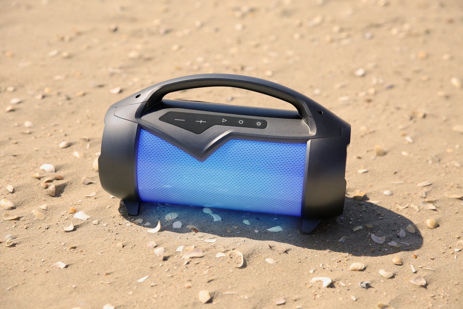 Een draagbare luidspreker met blauw licht staat op zand en schelpen op het strand.