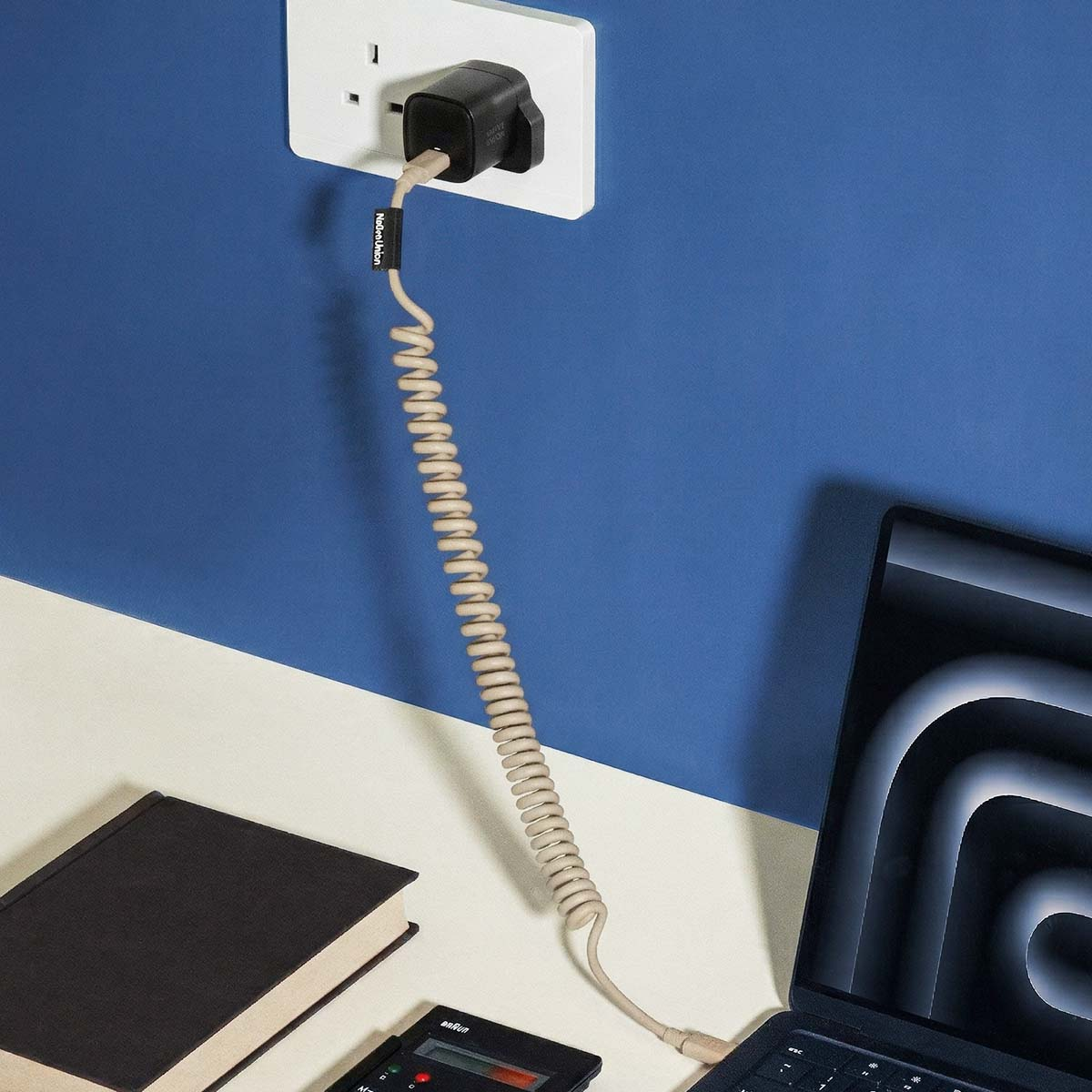 Un adaptateur secteur branché dans une prise murale, avec un câble en spirale relié à un ordinateur portable.