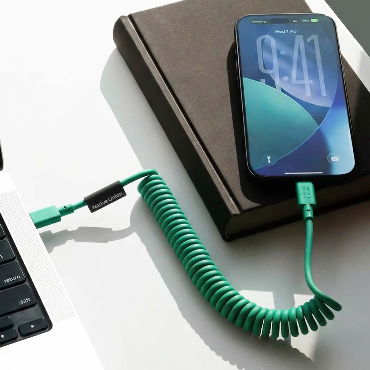 Un cavo verde a spirale collega un laptop a uno smartphone appoggiato su un libro.