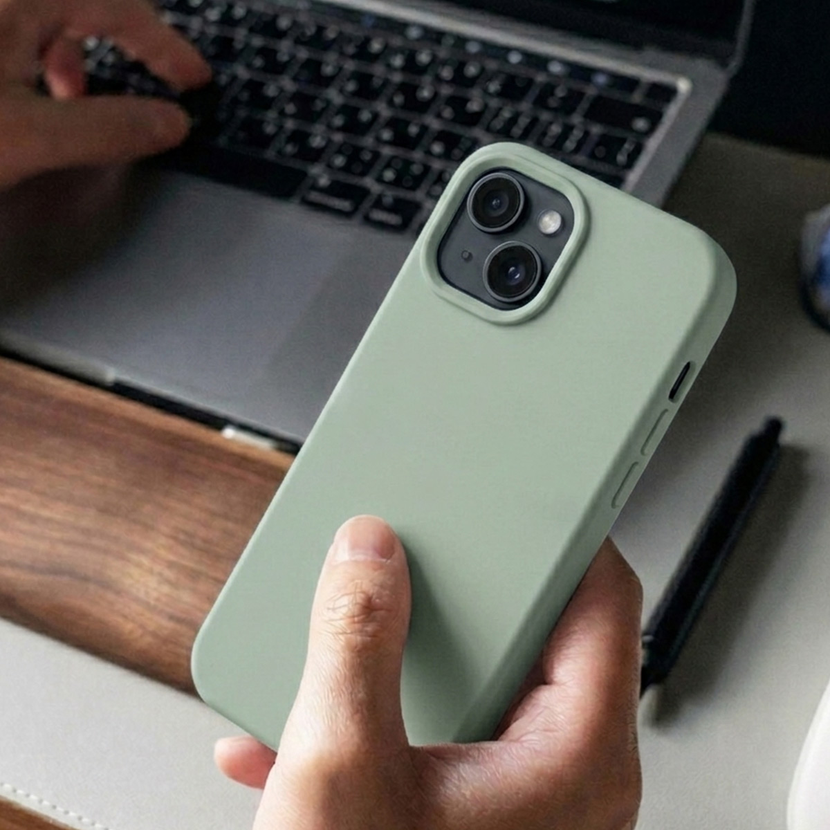 Une personne tient un téléphone vert clair devant un ordinateur portable. Des mains tapent sur le clavier.
