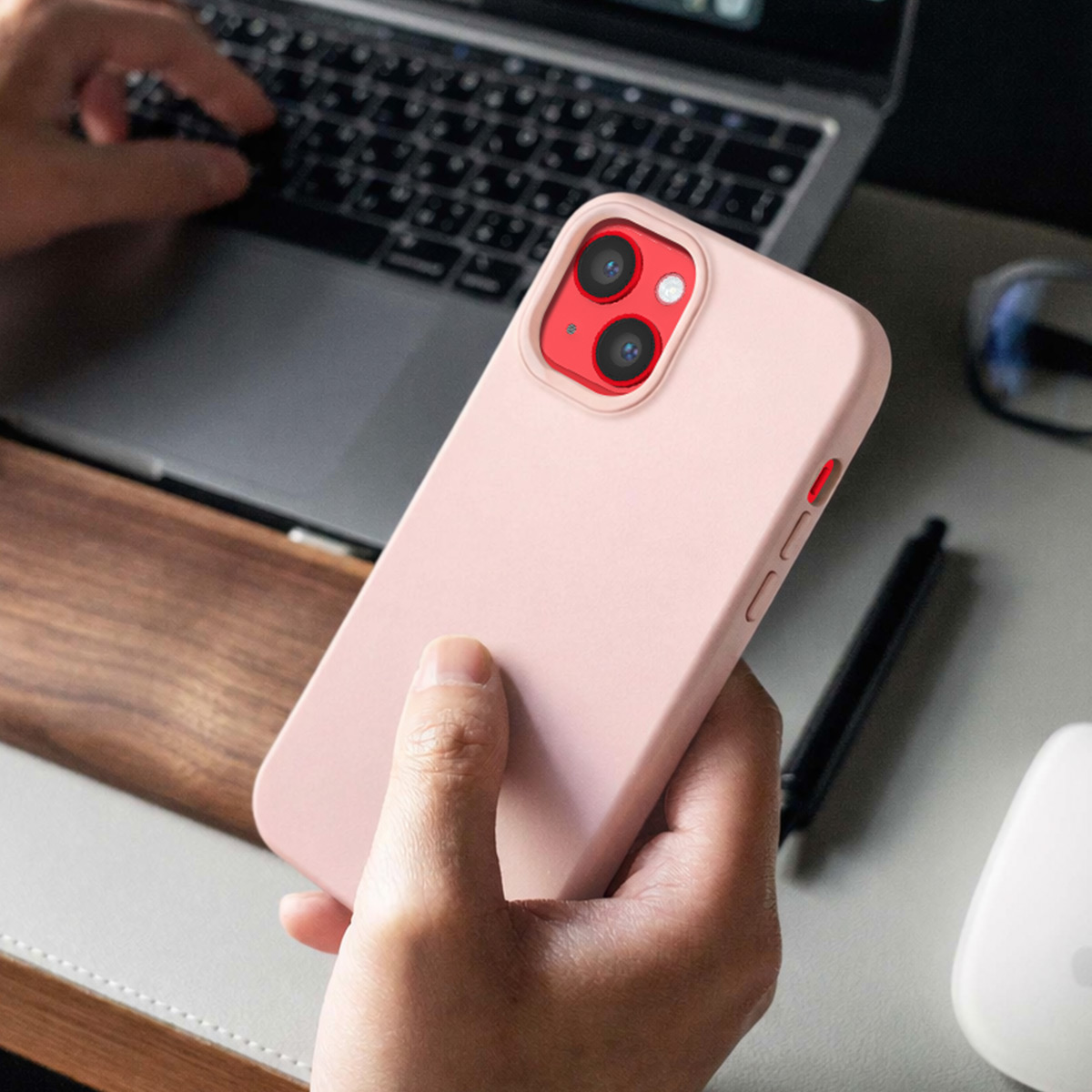 Eine Person hält ein rosa iPhone mit roter Kameraeinfassung vor einem Laptop.