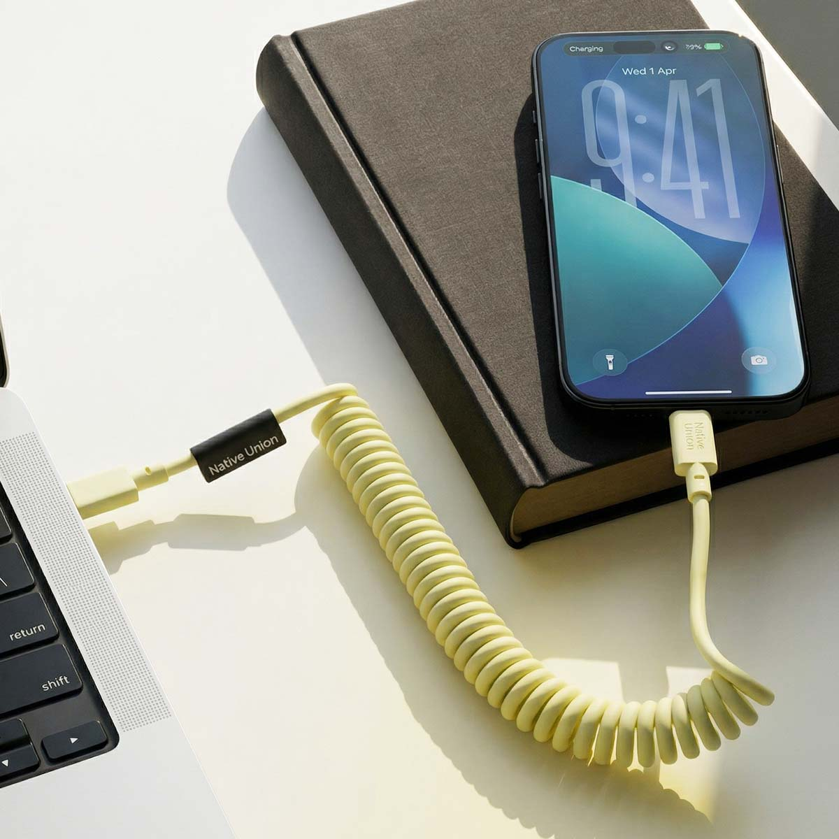 Un câble jaune en spirale relie un ordinateur portable à un iPhone posé sur un livre.