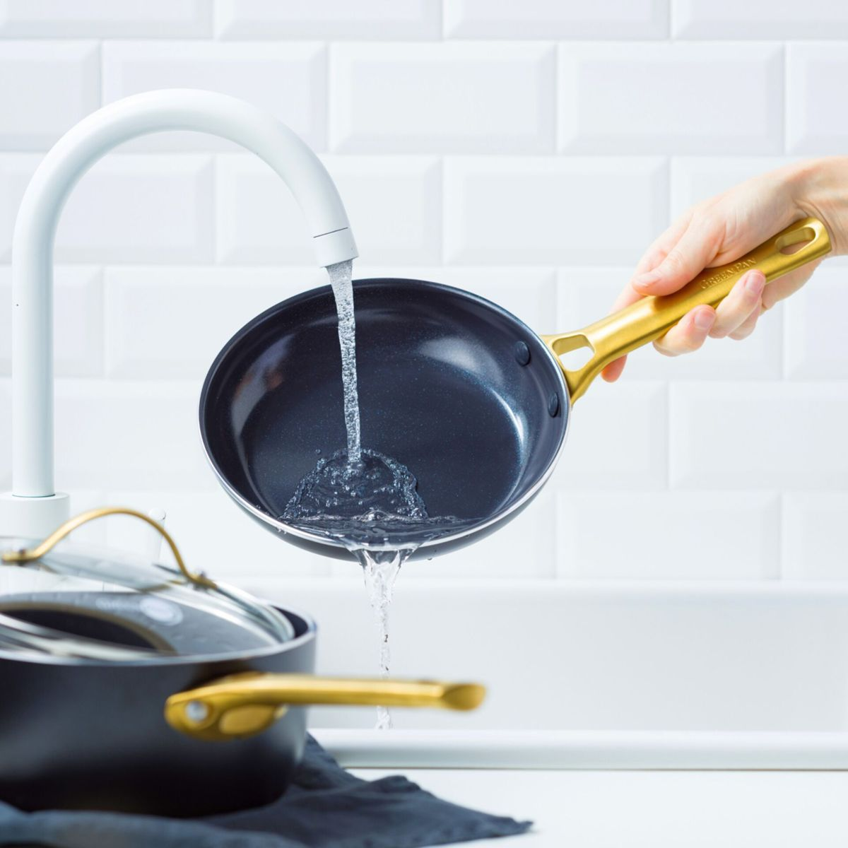 Eine Hand hält eine Pfanne unter fließendem Wasser in einer Spüle.