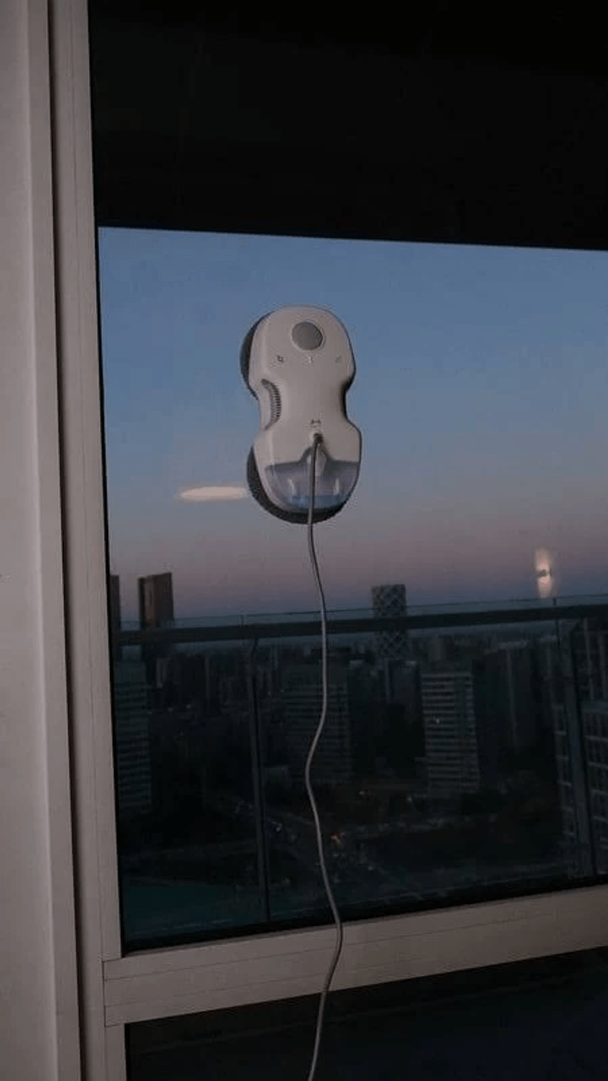 Un nettoyeur de vitres robotisé s'accroche à une fenêtre surplombant une ville au coucher du soleil.