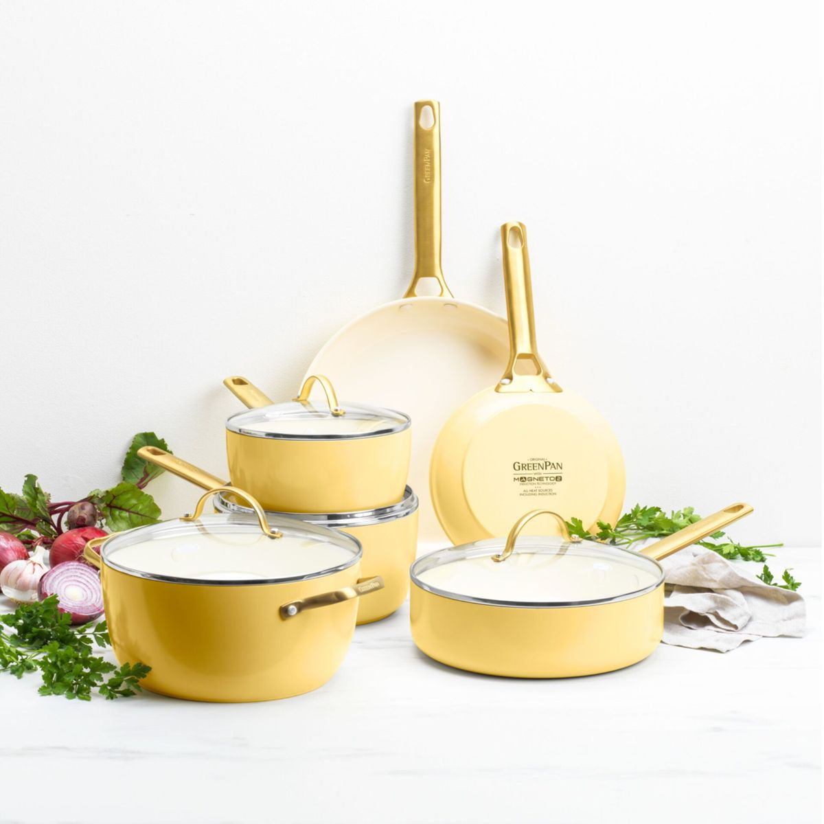 Gelbe Kochgeschirr-Set mit goldenen Griffen, daneben Gemüse wie Rote Bete und Zwiebeln.