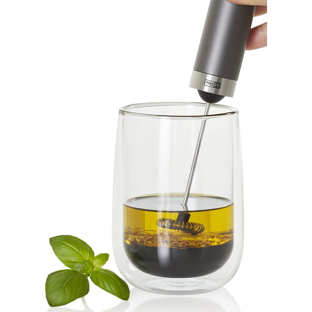 Un batteur à main mélange huile et balsamique dans un verre. Du basilic est à côté.