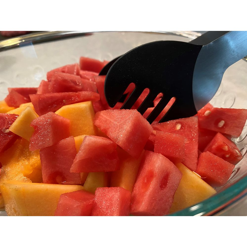 Ein Glas mit gewürfelter Wassermelone und Honigmelone, gehalten von schwarzen Zangen.