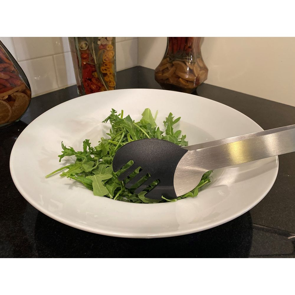 Ein Salatbesteck aus Metall und Kunststoff greift in eine Schüssel mit Rucola-Salat.