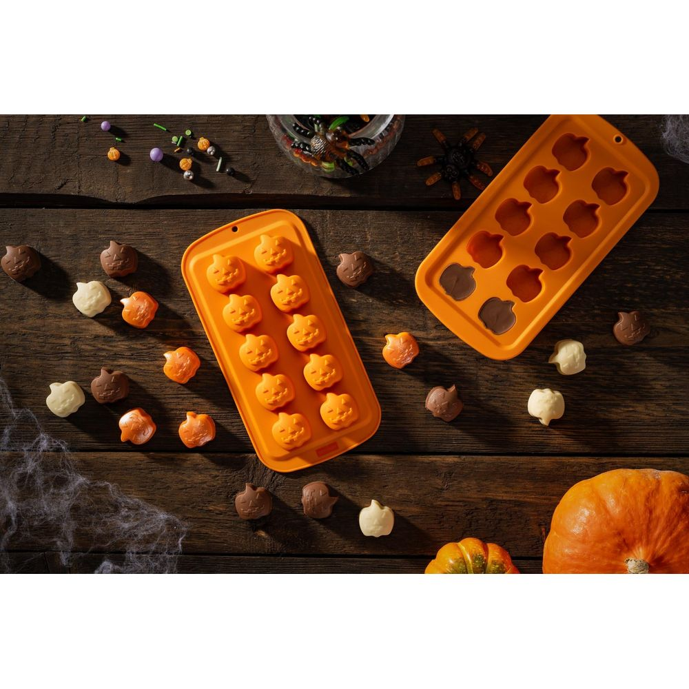 Zwei orangefarbene Halloween-Kürbis-Schokoladenformen liegen auf Holz.