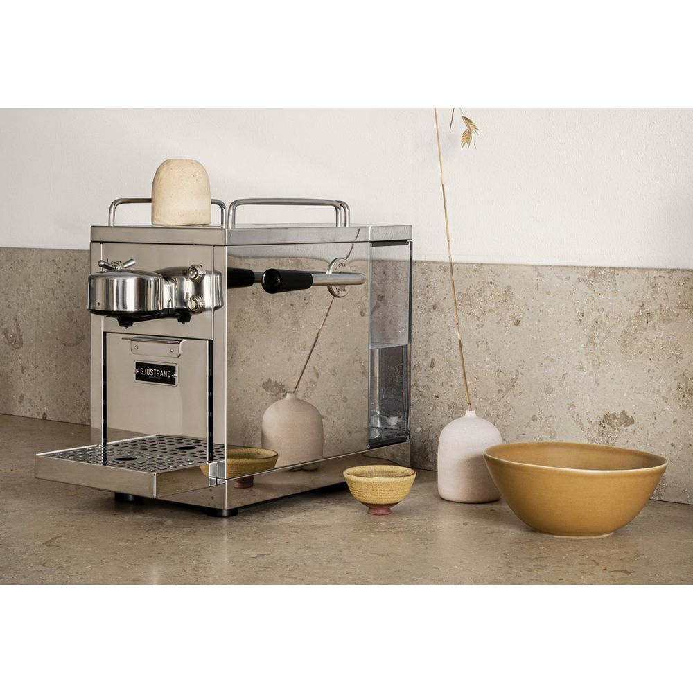 Eine schlanke Chrom-Espressomaschine steht auf einer Arbeitsplatte mit zwei dekorativen Vasen und Schalen.
