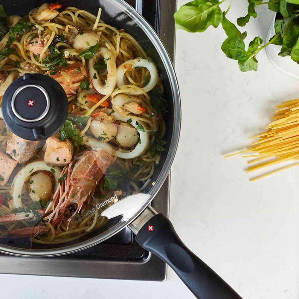 Spaghetti aux fruits de mer, saumon, crevettes et calamars dans une poêle. Spaghetti crus et basilic à proximité.