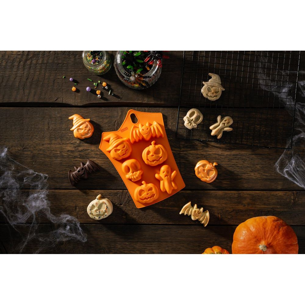 Halloween-Backutensilien mit Kürbis-, Geist- und Fledermausformen auf Holztisch.