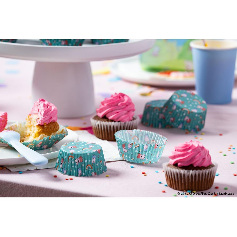 Dekorative Cupcake-Förmchen mit rosa Zuckerguss und Tiermotiven auf rosa Tischdecke.