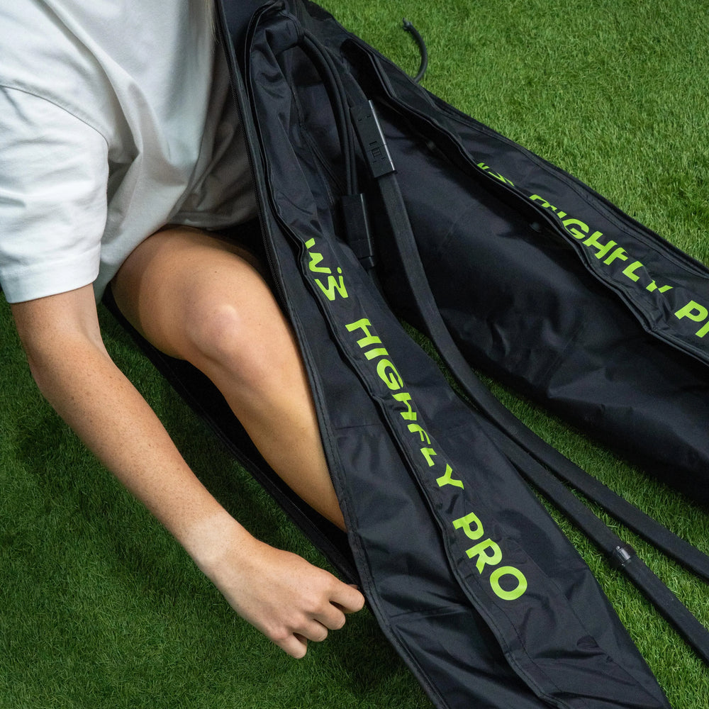 Una persona abre con cremallera una bolsa deportiva negra sobre césped artificial.