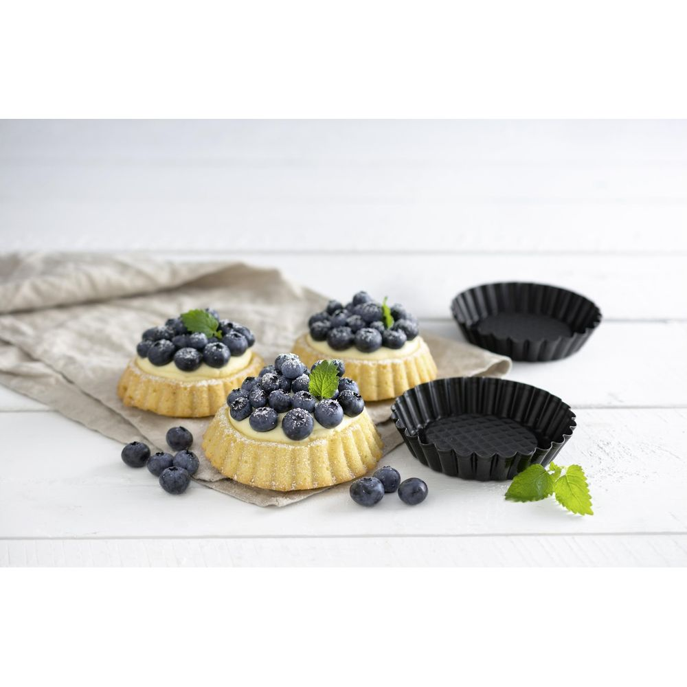 Drei Blaubeertörtchen auf einem Tuch, daneben zwei leere Tarteformen.