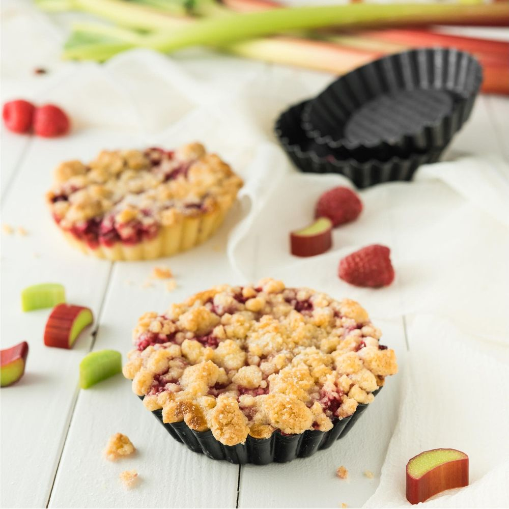 Zwei kleine Obstkuchen mit Streuseln und Himbeeren auf einem Holztisch.