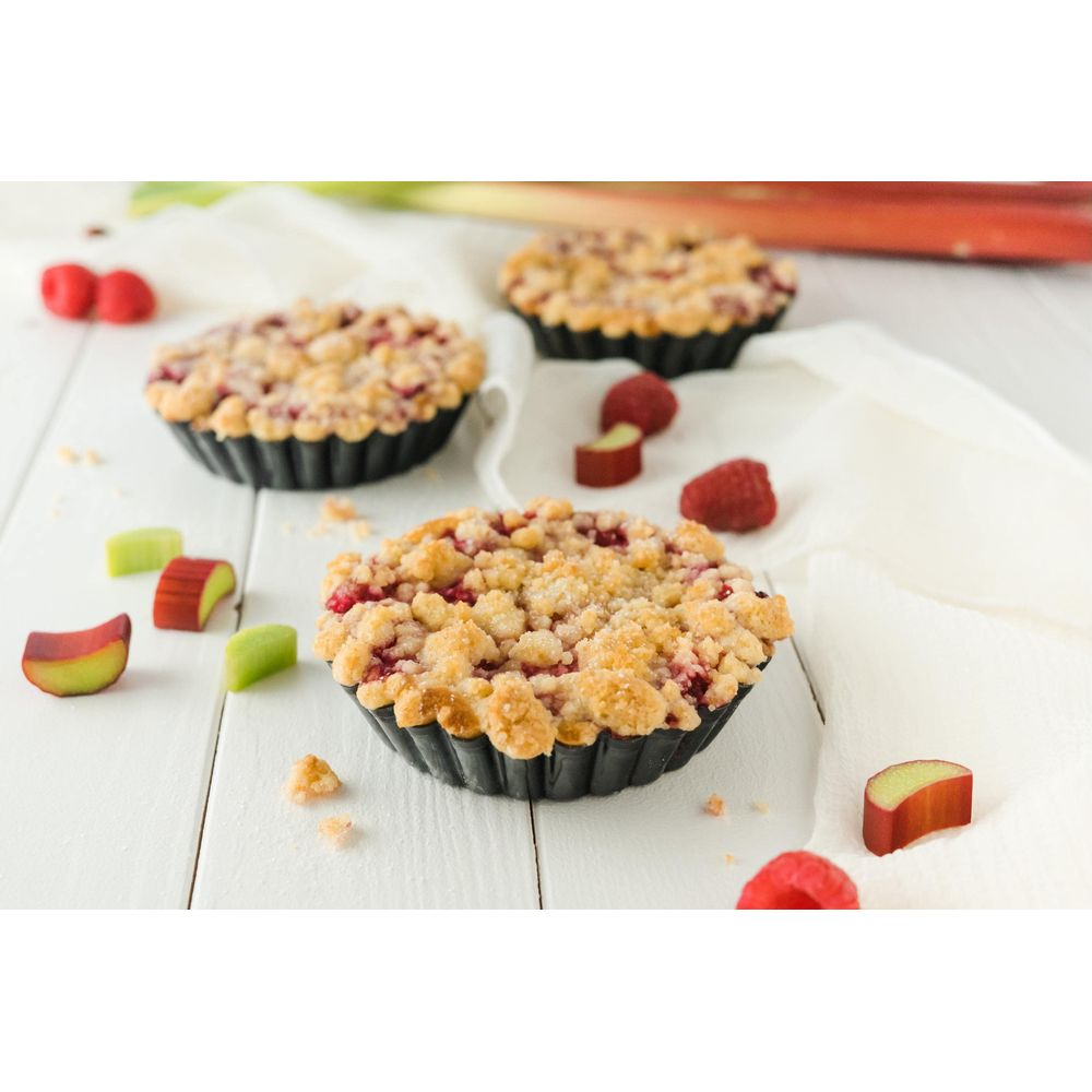 Drei kleine Obstkuchen mit Streuseln, Himbeeren und Rhabarberstücken auf weißem Holz.