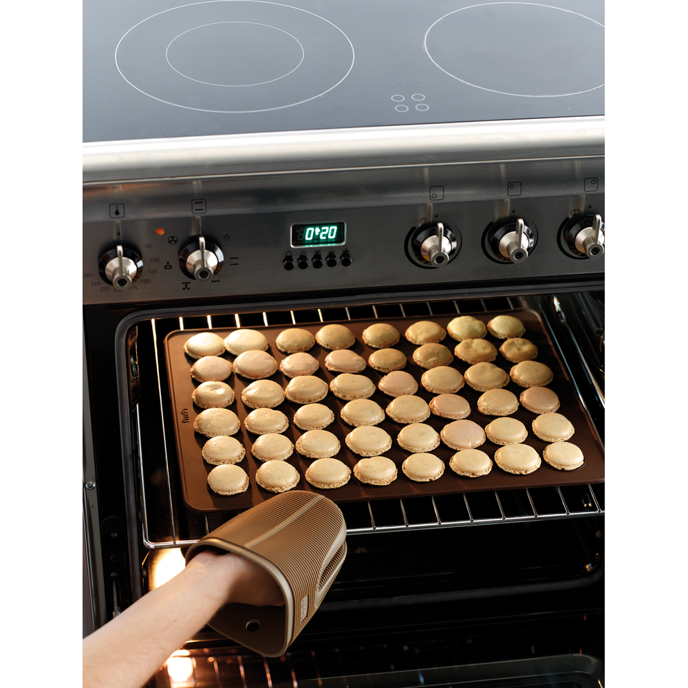 Une plaque de cuisson de nombreux macarons est retirée d'un four.