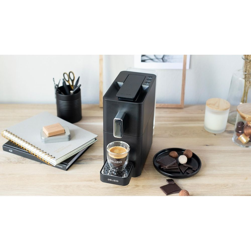Una macchina da caffè nera con un bicchiere di espresso, cioccolatini e caramelle.