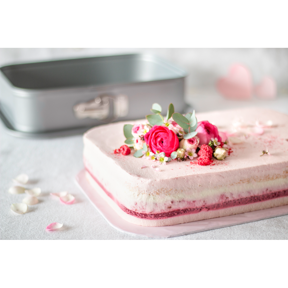 Ein rosa Kuchen mit Blumen und Himbeeren, neben einer Backform.