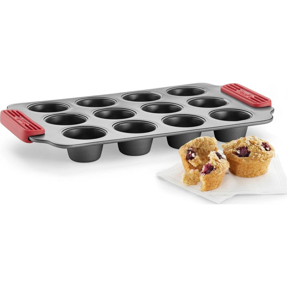 Un moule à 12 mini-muffins avec poignées rouges, à côté se trouvent deux muffins.