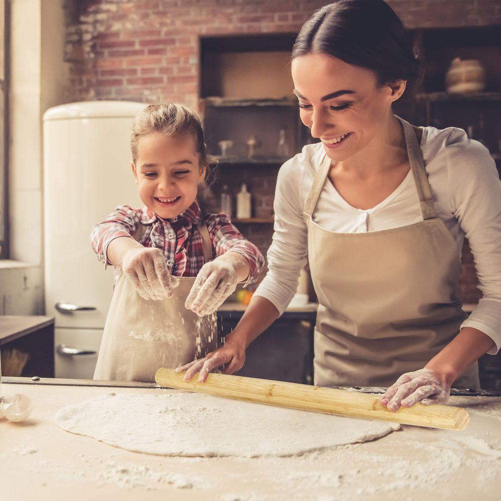 Mutter und Kind backen zusammen in einer Küche, sie rollen Teig aus.
