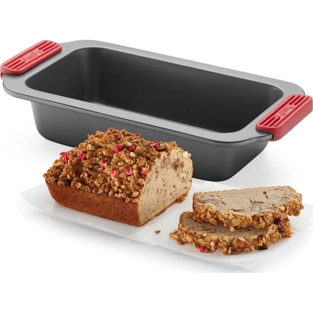 Ein Brotlaib mit Kruste und Scheiben neben einer Backform mit roten Griffen.