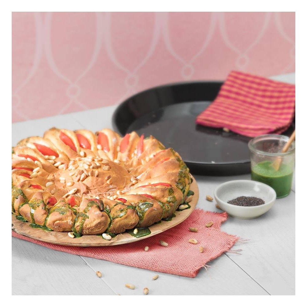 Pain en forme de fleur avec tomates et pignons sur assiette en bois, à côté d'une sauce verte.