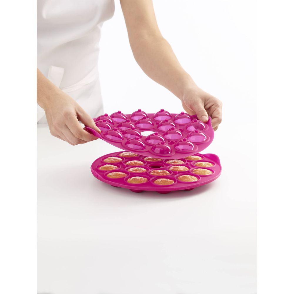 Eine Person hält eine runde, pinke Silikonform mit kleinen runden Kuchen.