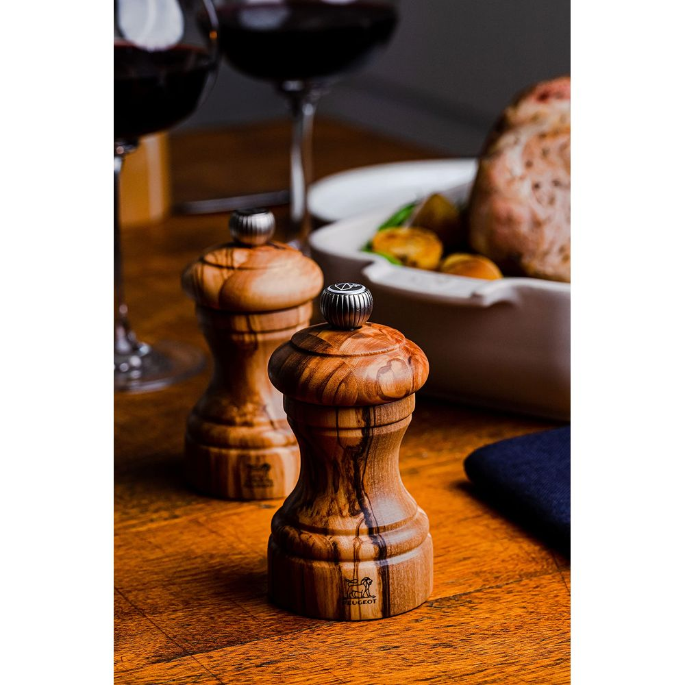 Due macina sale e pepe in legno su un tavolo di legno con cibo sullo sfondo.