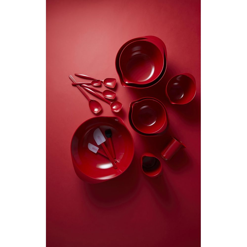 Utensili da cucina rossi, tra cui ciotole, cucchiai e spatole, su sfondo rosso.