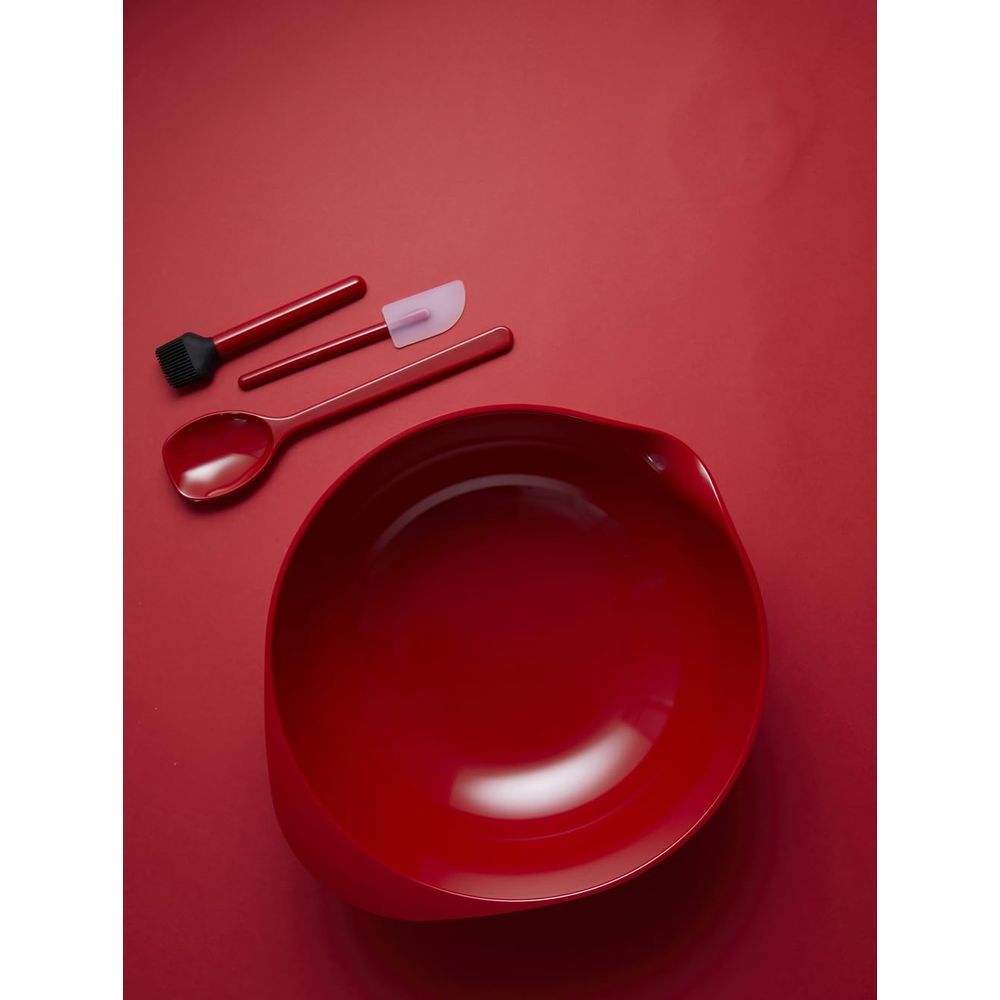 Ciotola rossa con cucchiaio, pennello e spatola su sfondo rosso.