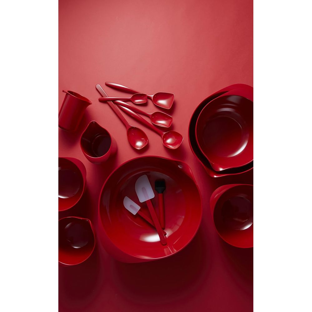 Set di utensili da cucina rossi: ciotole, cucchiai, spatole e misurini su sfondo rosso.