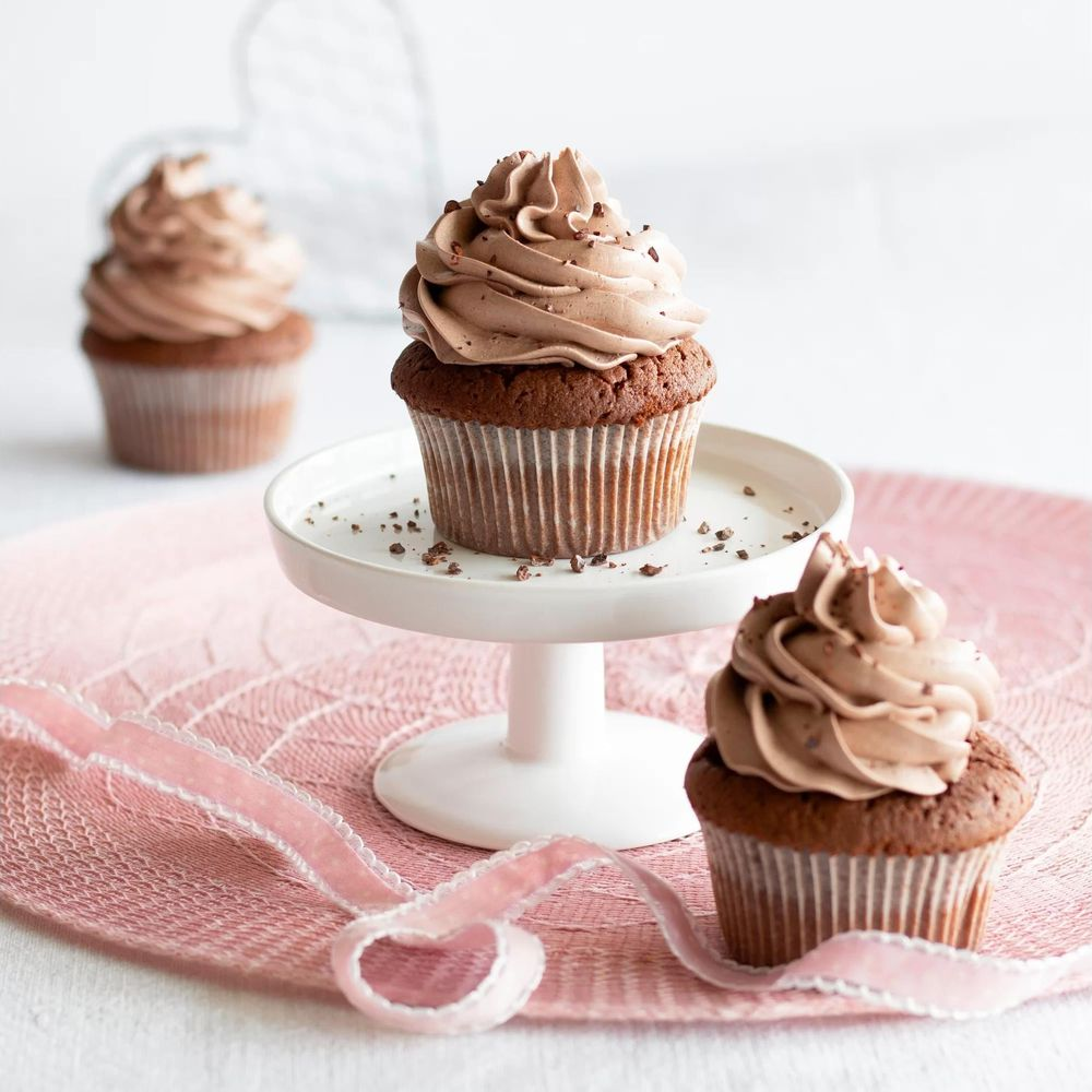Drei Schokoladen-Cupcakes mit Schokoladencreme-Topping auf einem rosa Untersetzer.