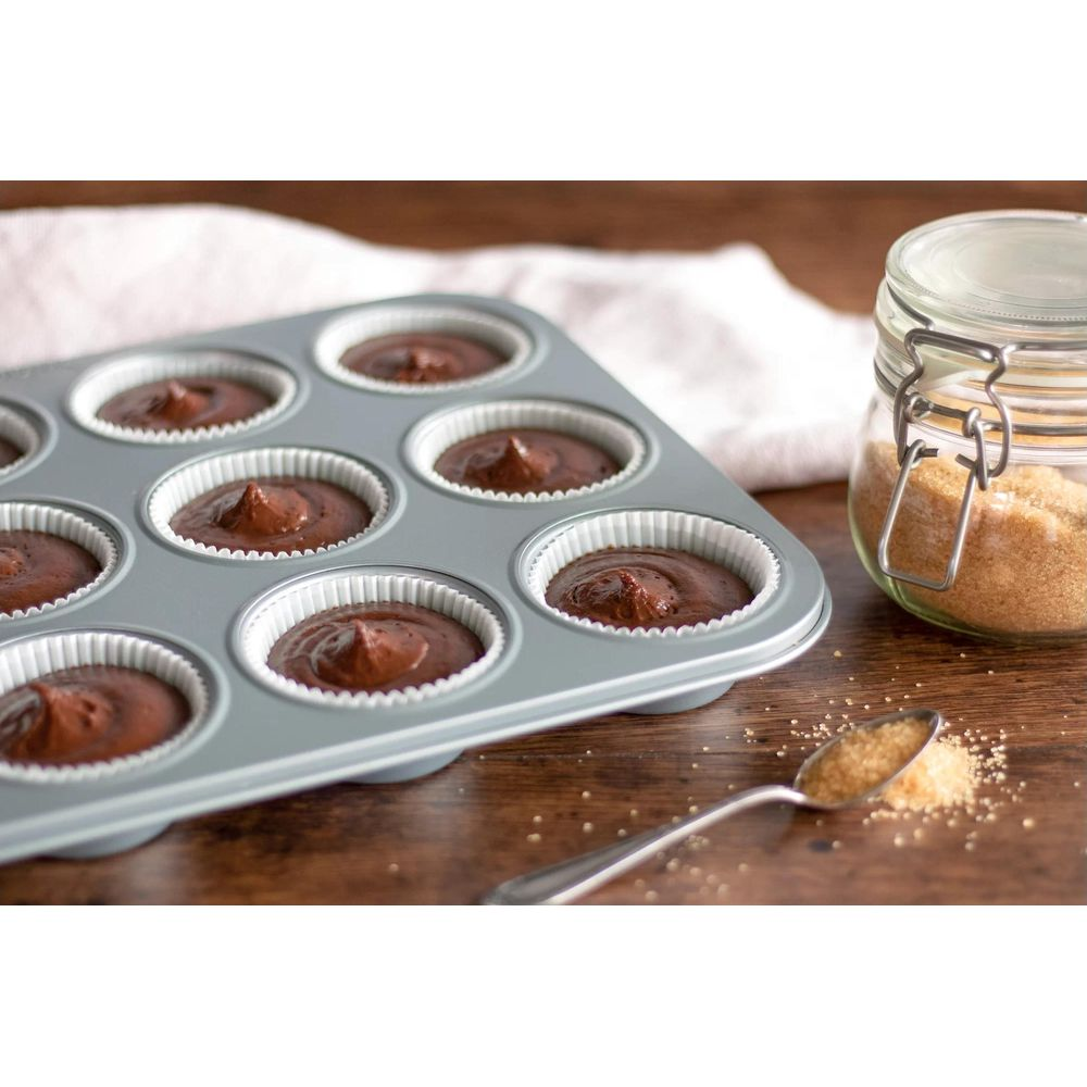 Schokoladenmuffin-Teig füllt eine Muffinform, daneben Zucker und ein Löffel.