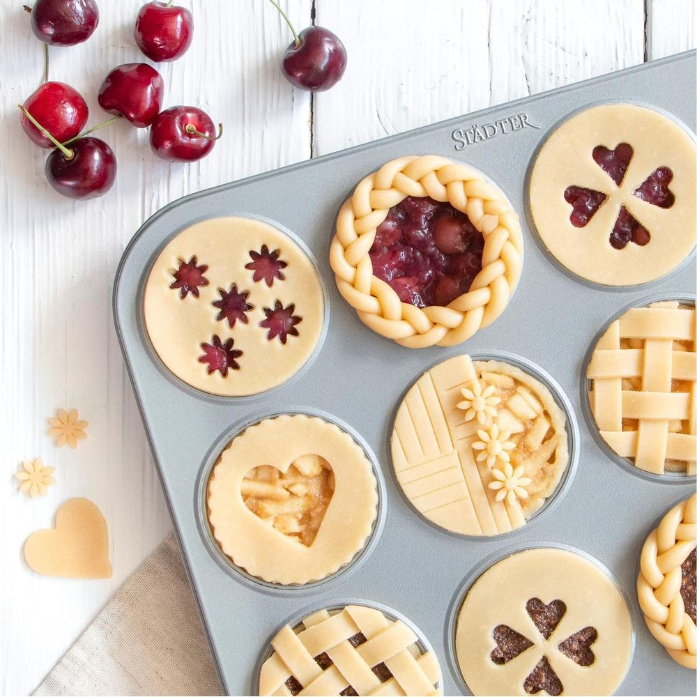 Kleine Kuchen mit verschiedenen Mustern und Kirschen auf einem Tisch.