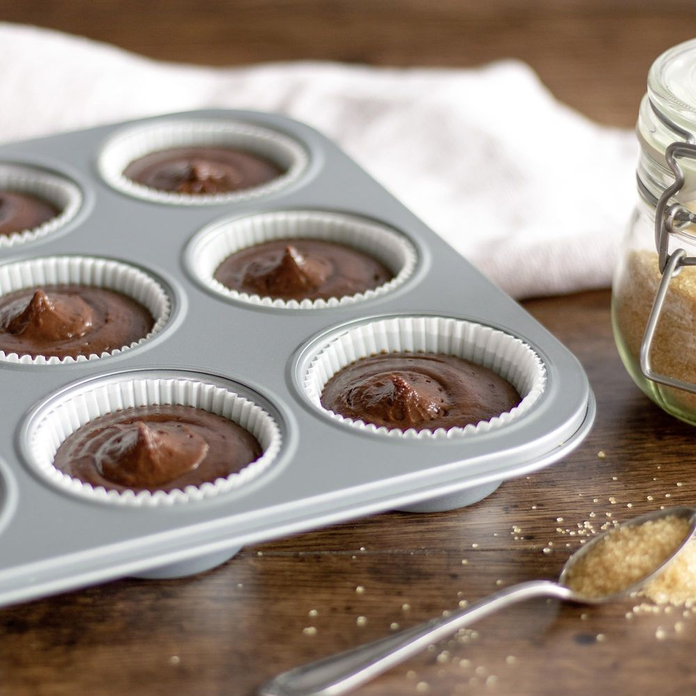 Schokoladenkuchenteig in einer Muffin-Form, neben braunem Zucker und einem Löffel.