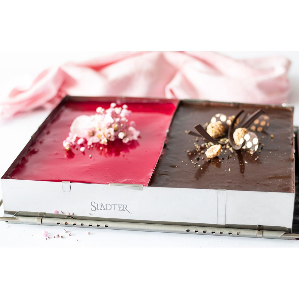 Ein eckiger Kuchen mit Beeren- und Schokoladenhälften, garniert mit Blumen und Nüssen.