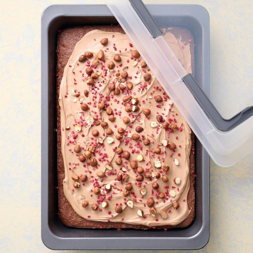 Schokoladenkuchen mit heller Glasur, Nüssen und Himbeeren in einer Backform.