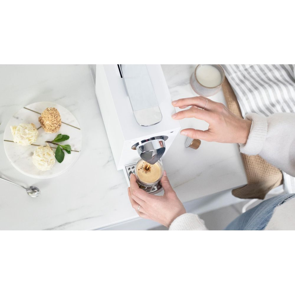 Eine Person macht einen Espresso in einer weißen Maschine. Links sind drei Pralinen.