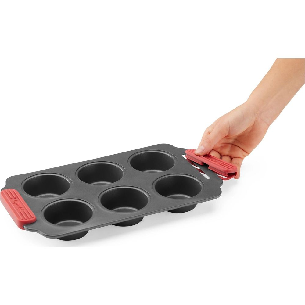Eine Hand hält den roten Griff einer dunklen 6-Muffin-Backform.